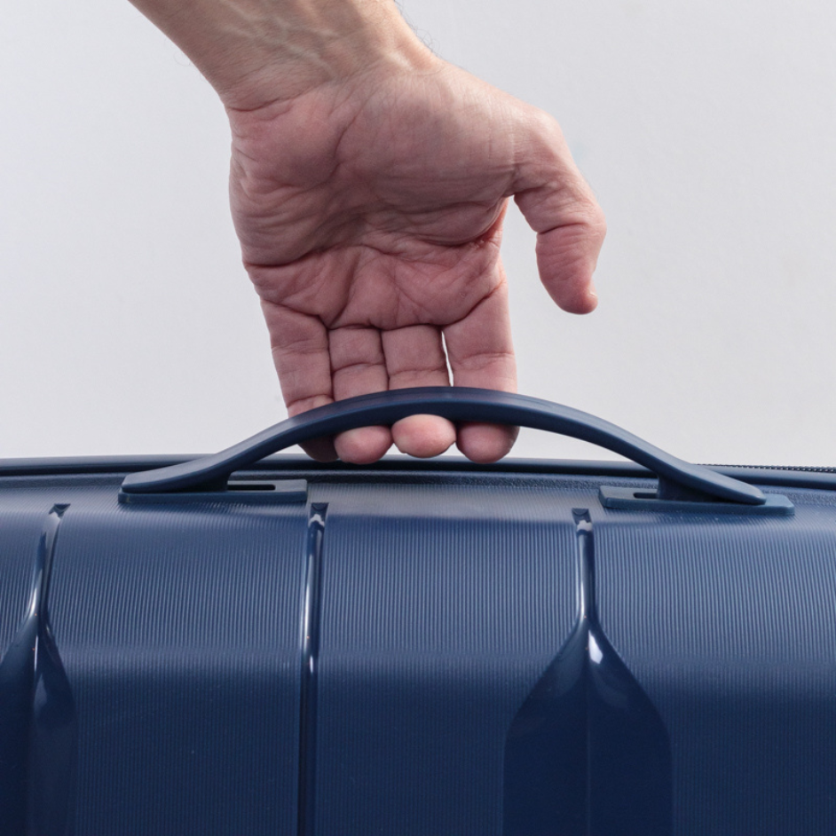 Mano sujetando el asa lateral de una valija azul, mostrando su diseño ergonomico y textura.