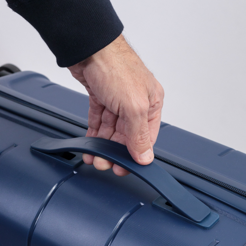 Mano sujetando el asa superior de una valija azul, destacando el diseño del agarre y textura.